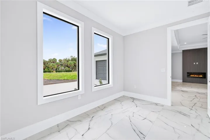 Spare room with a large fireplace, light marble finish flooring, and crown molding
