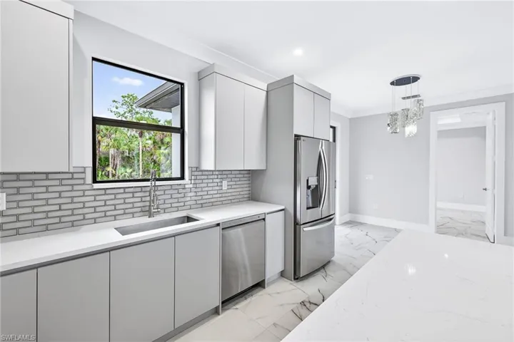 Kitchen with modern cabinets, hanging light fixtures, light marble finish floors, stainless steel appliances, and light stone counters