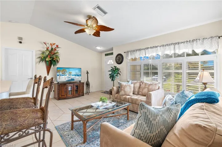 Living room with ceiling fan, light tile patterned floors, and vaulted ceiling