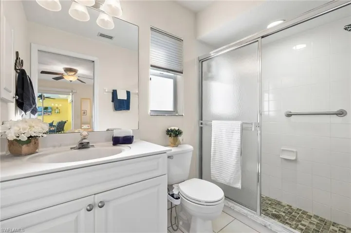 Bathroom featuring vanity, a shower with door, tile patterned floors, ceiling fan, and toilet