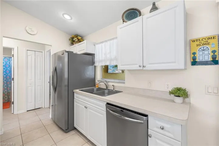 Kitchen with lofted ceiling, sink, light tile patterned floors, appliances with stainless steel finishes, and white cabinetry