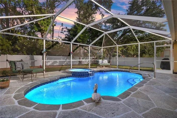 Pool at dusk featuring a lanai, a patio area, and an in ground hot tub