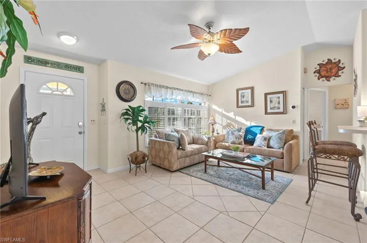 Living room featuring ceiling fan, lofted ceiling, and light tile patterned flooring