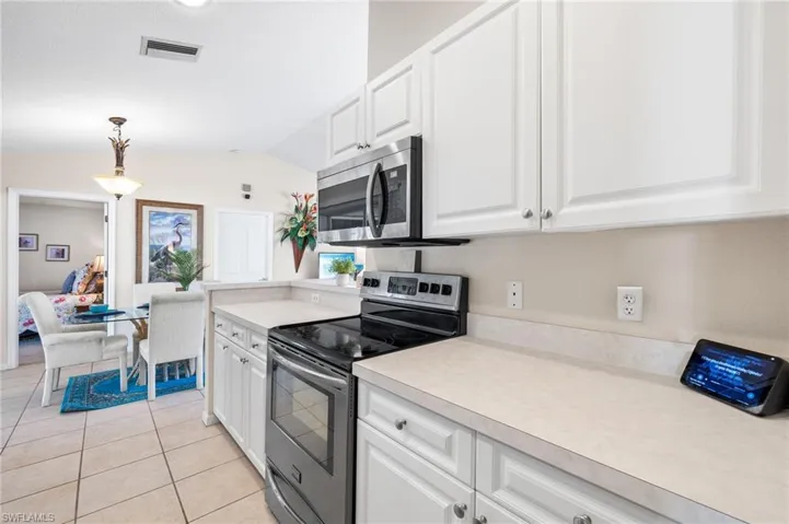 Kitchen with appliances with stainless steel finishes, light tile patterned floors, white cabinets, hanging light fixtures, and lofted ceiling