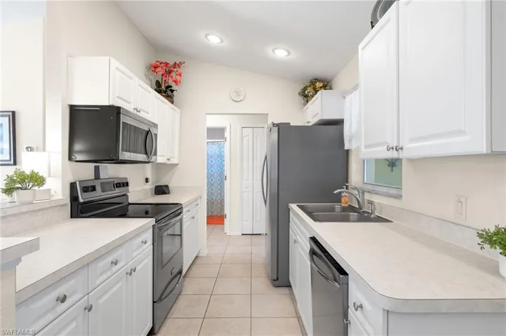 Kitchen featuring white cabinetry, light tile patterned floors, lofted ceiling, and appliances with stainless steel finishes