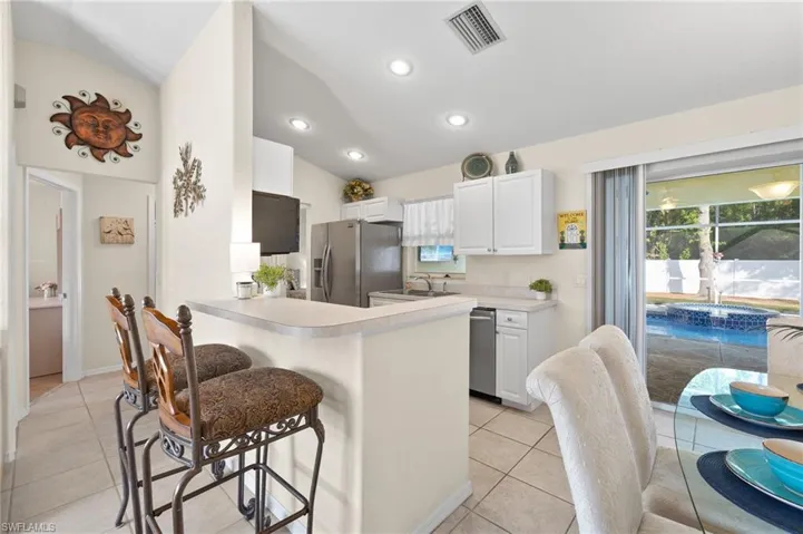 Kitchen featuring white cabinetry, stainless steel appliances, kitchen peninsula, lofted ceiling, and light tile patterned floors