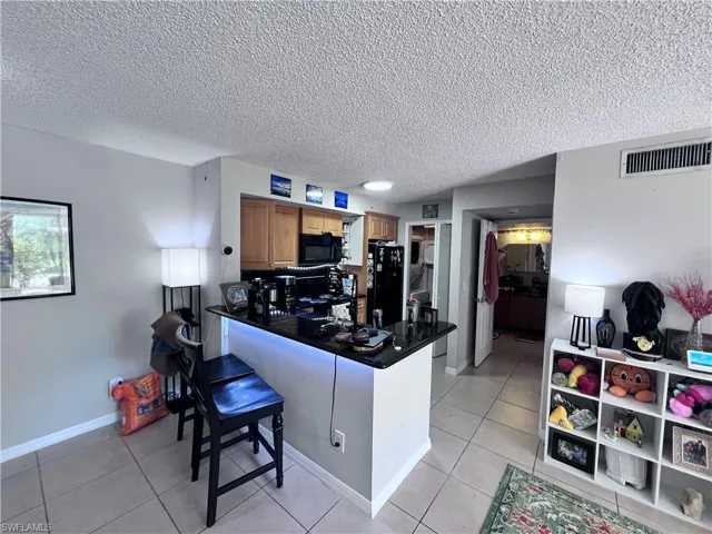 Kitchen featuring wood finish cabinetry, dark countertops, a textured ceiling, a kitchen bar, and black appliances