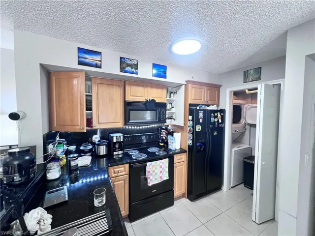Kitchen featuring black appliances, a textured ceiling, stacked washer / drying machine, light tile patterned floors, and backsplash