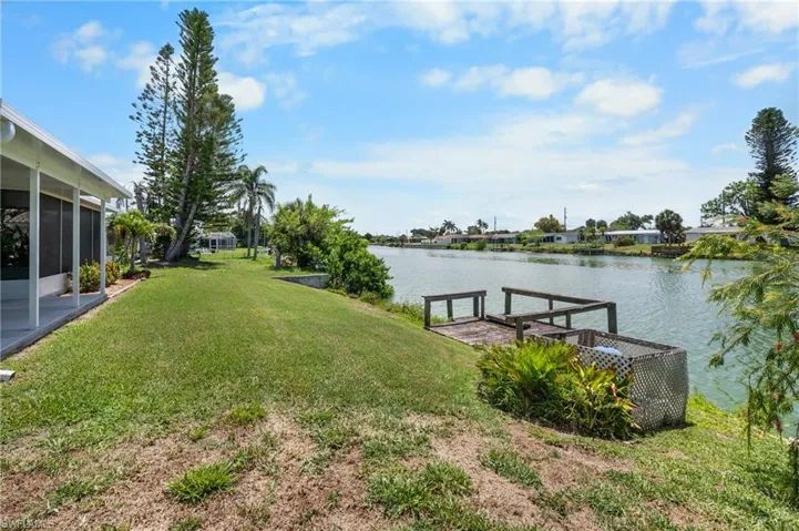 Waterfront property featuring a private wooden dock, expansive green lawn, mature trees, and a screened-in porch