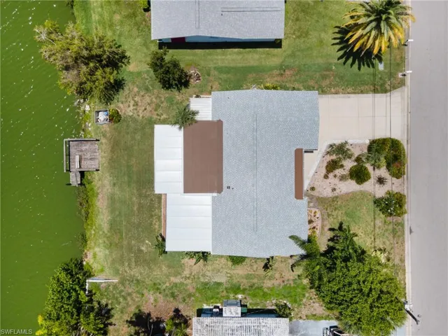 Waterfront property featuring a private wooden dock, mature trees, a paved driveway, and established landscaping