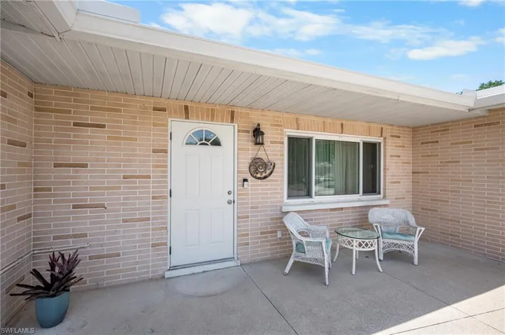 Covered concrete patio entrance featuring a white arched paneled door, light brick exterior, and a horizontal window
