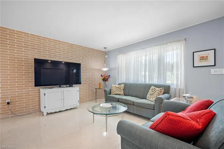 Living space featuring a full brick accent wall, light-toned flooring, and a large window with sheer drapes