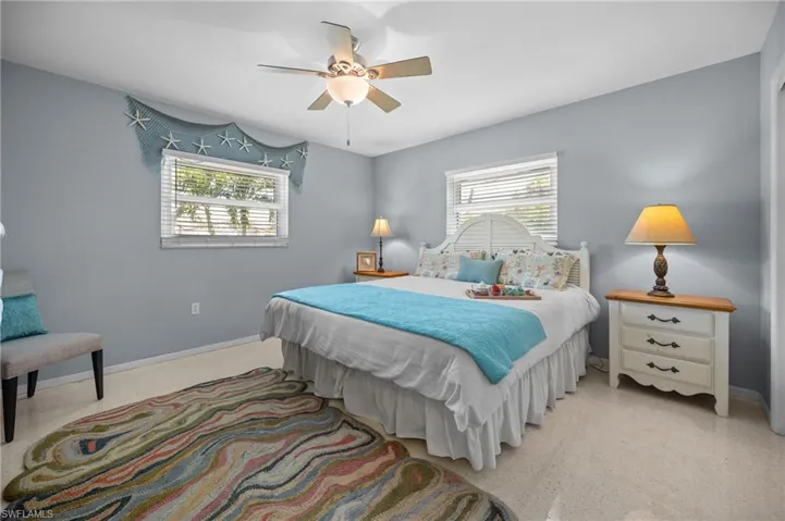 Bedroom featuring light blue wall paint, a ceiling fan with integrated lighting, two windows with blinds, and light-colored flooring
