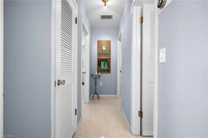 Hallway with light blue walls, speckled flooring, white louvered doors, and recessed lighting