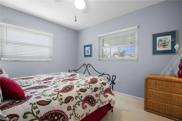 Bedroom featuring light blue walls, two windows with horizontal blinds, and a ceiling fan with light fixture