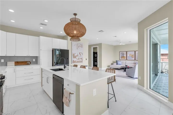 Kitchen featuring white cabinetry, sink, an island with sink, decorative light fixtures, and appliances with stainless steel finishes /  virtually enhanced photo