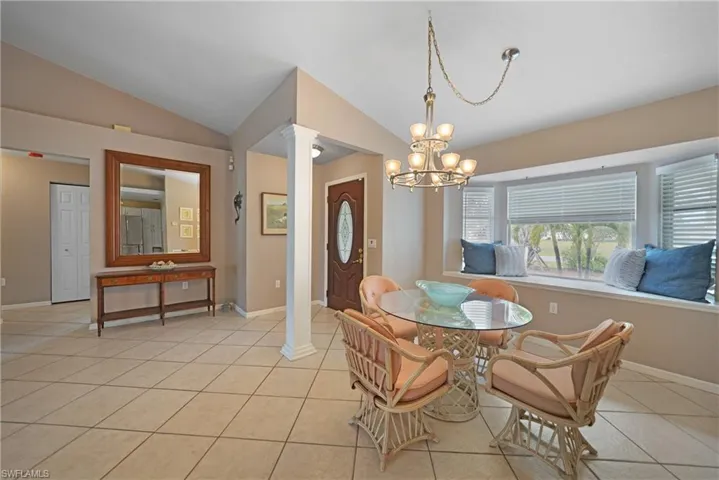 Tiled dining space with decorative columns, a notable chandelier, and vaulted ceiling