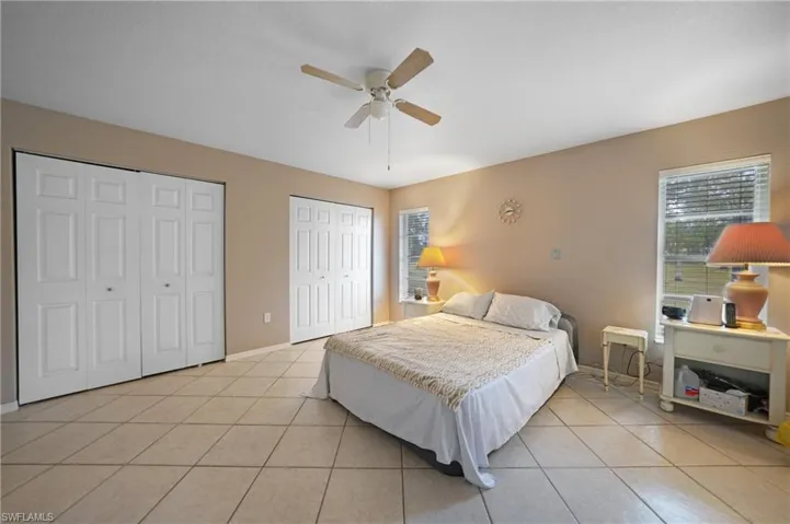 Tiled master bedroom with multiple closets, ceiling fan, and multiple windows