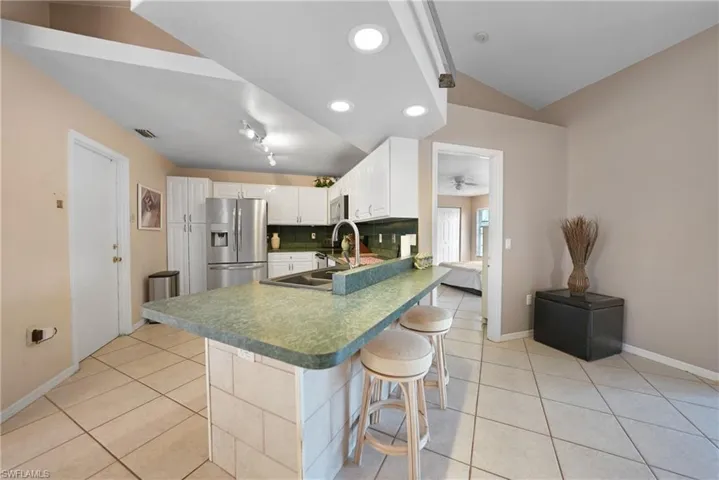 Kitchen with appliances with stainless steel finishes, lofted ceiling, a kitchen bar, white cabinetry, and sink