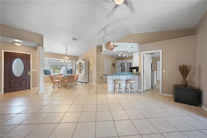 Kitchen featuring kitchen peninsula, stainless steel fridge, white cabinetry, light tile patterned floors, and lofted ceiling