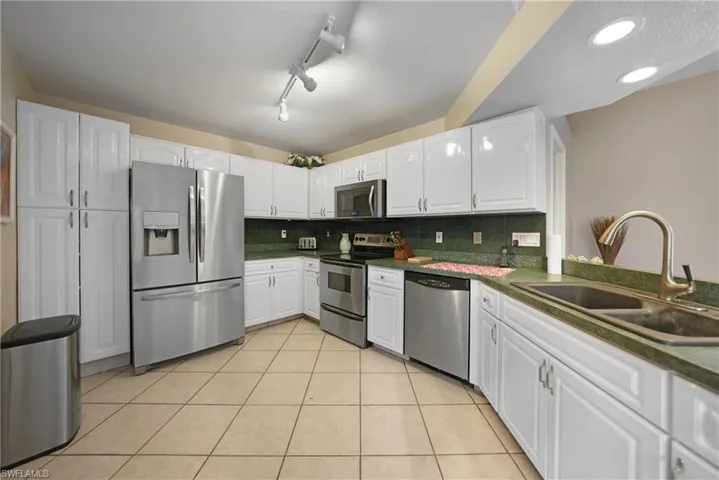 Kitchen featuring white cabinetry, decorative backsplash, sink, stainless steel appliances, and light tile patterned flooring