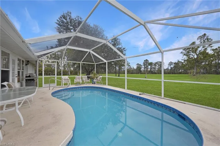 View of pool with screen enclosure, a patio area, a yard, and grilling area