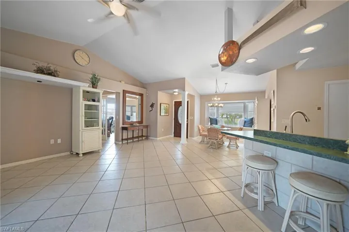 Kitchen featuring a kitchen bar, light tile patterned floors, decorative light fixtures, ceiling fan with notable chandelier, and lofted ceiling