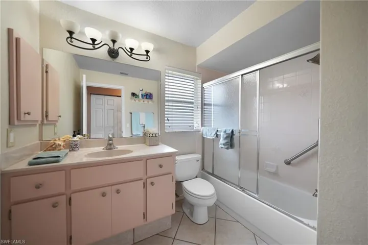 Full bathroom featuring tile patterned floors, enclosed tub / shower combo, a textured ceiling, toilet, and vanity
