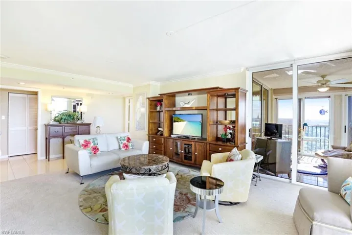 Living room with a ceiling fan, plenty of natural light, light colored carpet, and crown molding