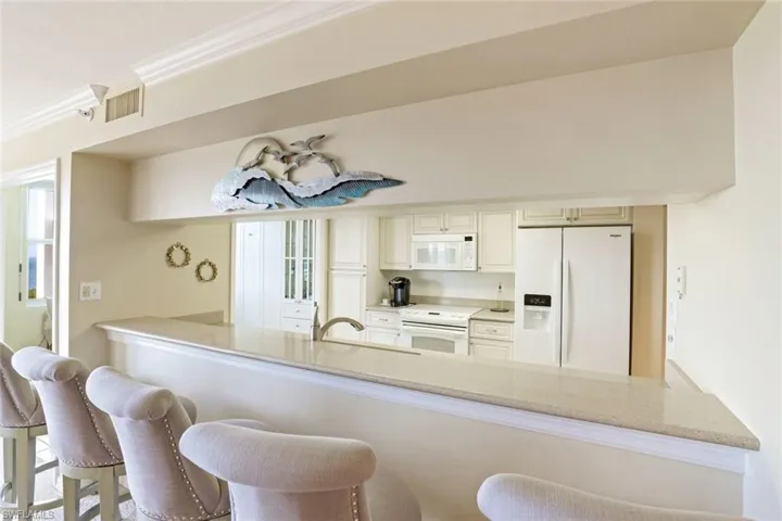 Kitchen featuring a peninsula, white appliances, crown molding, a kitchen bar, and light stone countertops