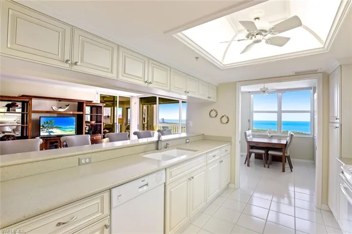 Kitchen with a ceiling fan, white appliances, a skylight, cream cabinets, and light tile patterned flooring