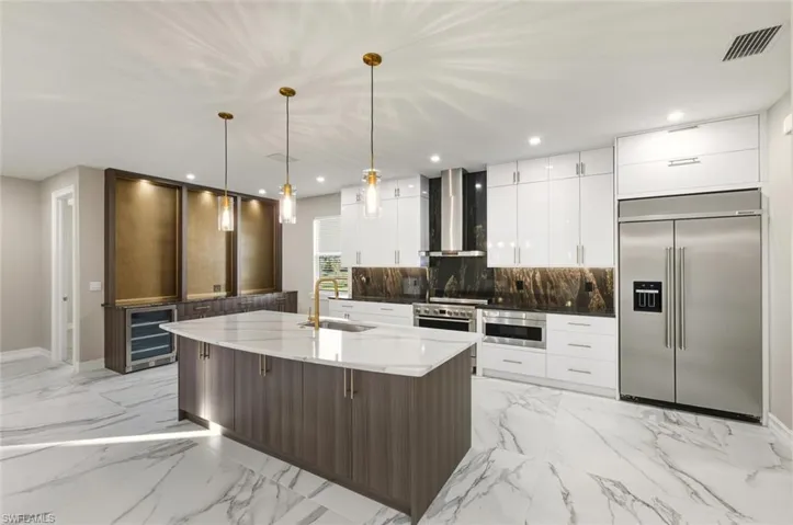 Two tone kitchen featuring dark stone counters, premium appliances, modern cabinets, beverage cooler, and a center island with sink
