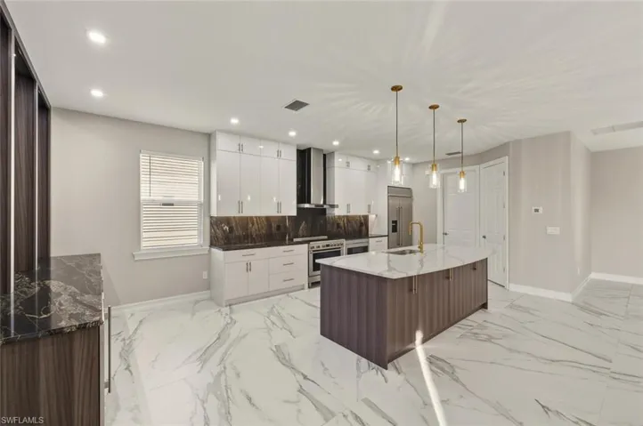 Two tone kitchen with dark stone countertops, high quality appliances, two tone color scheme, pendant lighting, and light marble finish flooring