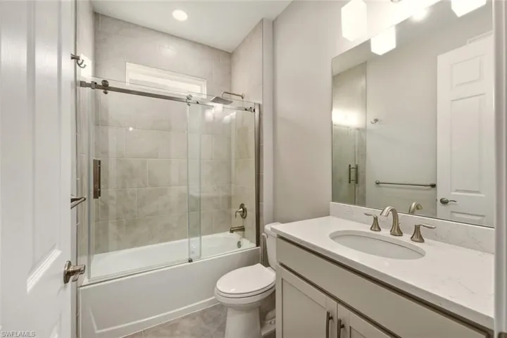 Bathroom featuring vanity, enclosed tub / shower combo, recessed lighting, and light tile patterned floors