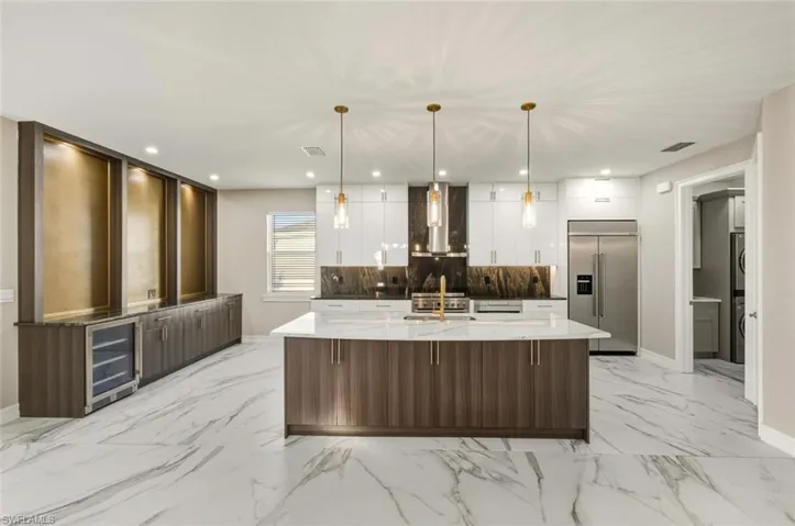 Kitchen featuring light stone counters, modern cabinets, stainless steel appliances, two tone cabinets, and hanging light fixtures