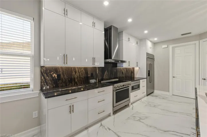 Kitchen featuring white cabinetry, built in appliances, light marble finish floors, dark stone counters, and recessed lighting