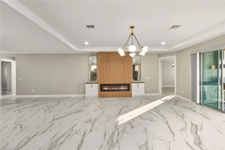 Kitchen featuring a fireplace, a tray ceiling, suspended lighting, open floor plan, and light marble finish flooring