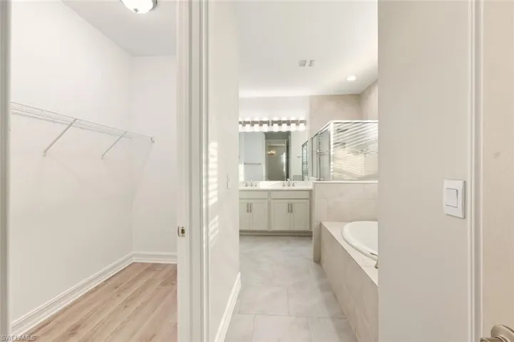 Bathroom featuring a stall shower, double vanity, a garden tub, light tile patterned flooring, and a spacious closet