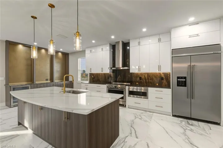 Kitchen with high quality appliances, modern cabinets, two tone color scheme, light stone countertops, and decorative light fixtures