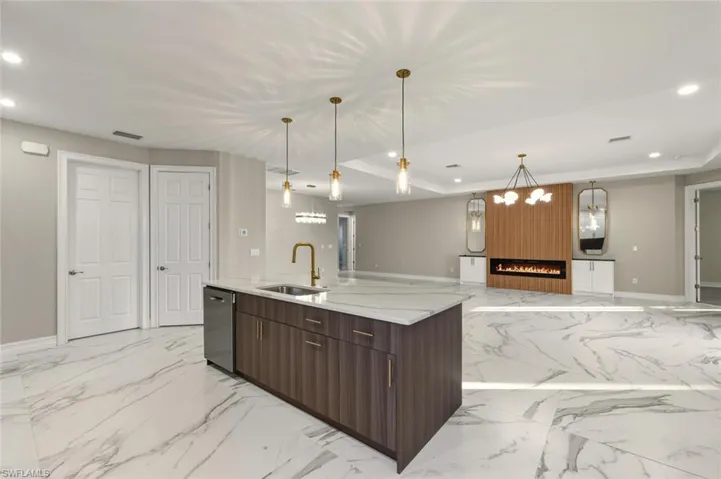 Kitchen featuring open floor plan, light stone countertops, a fireplace, dark wood finish cabinetry, and an island with sink