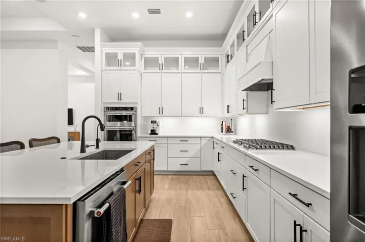 Kitchen with glass insert cabinets, white cabinetry, appliances with stainless steel finishes, recessed lighting, and a kitchen bar