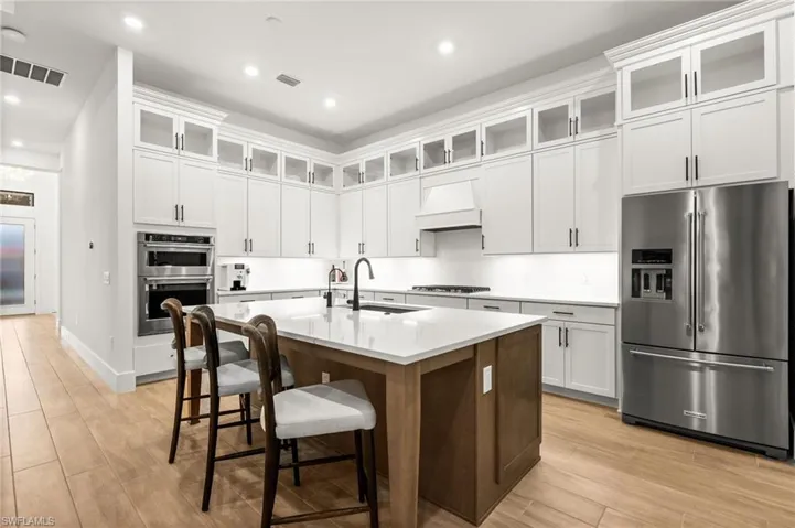Kitchen featuring glass insert cabinets, stainless steel appliances, white cabinets, a kitchen breakfast bar, and a center island with sink