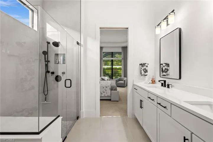 Ensuite bathroom with double vanity, a shower stall, light colored carpet, and light tile patterned floors