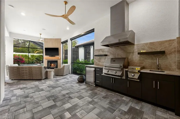 View of patio with a glass covered fireplace, ceiling fan, exterior kitchen, a sunroom, and a lanai