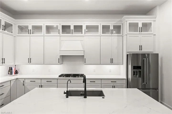 Kitchen featuring glass insert cabinets, high end fridge, light stone counters, white cabinets, and custom range hood