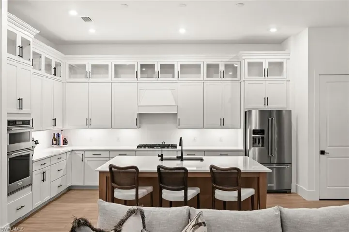 Kitchen featuring glass insert cabinets, appliances with stainless steel finishes, a kitchen breakfast bar, white cabinets, and a kitchen island with sink