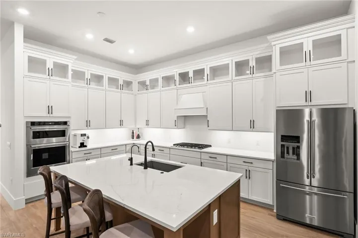 Kitchen featuring glass insert cabinets, stainless steel appliances, light stone counters, a breakfast bar, and an island with sink