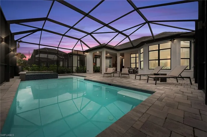 Pool at dusk featuring a sunroom, a lanai, a pool with connected hot tub, and a patio