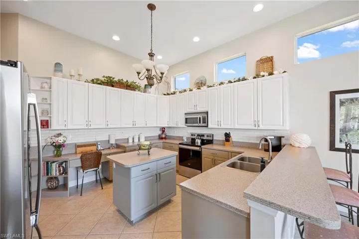 Kitchen featuring a peninsula, a sink, appliances with stainless steel finishes, a kitchen bar, and pendant lighting