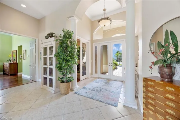 Foyer entrance with french doors, decorative columns, light tile patterned floors, a towering ceiling, and baseboards